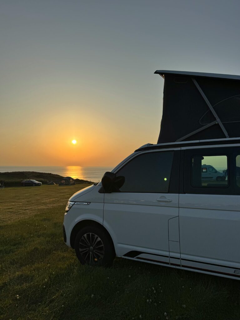 A camper van parked near the ocean during a stunning sunset, ideal for travel themes.